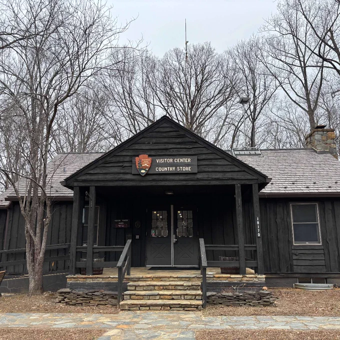 Rustic dark wooden visitor center and country store cabin with a stone porch and walkway surrounded by leafless trees