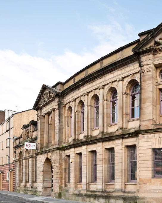 Historic sandstone building with arched windows and classical architectural details under a clear sky.