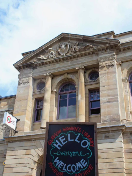 Historic stone building facade with tall columns and a colorful chalkboard sign reading 'Hello everyone welcome' at Glasgow Women's Library.