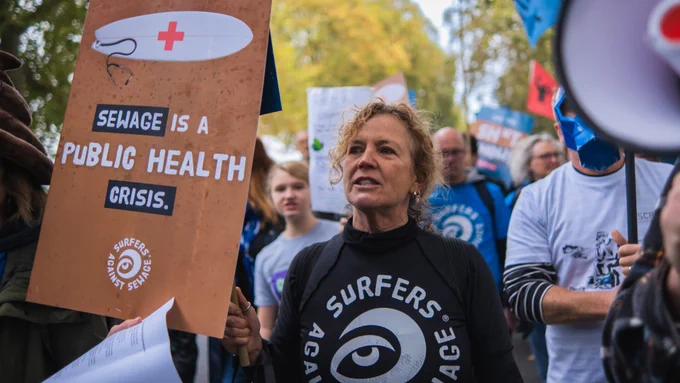 Image Credit: Surfers Against Sewage photo shows campaigner in wetsuit with poster stating Sewage is a public health crisis