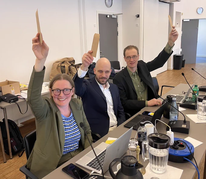 Diana, Mads og Erik sidder med en arm i vejret. I hånden holder de en brun kuvert med deres stemmer.