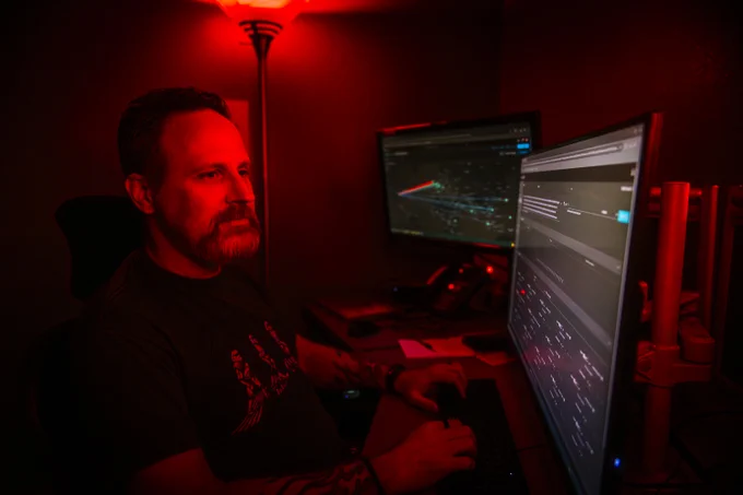 Person working in a dimly lit room with two monitors displaying data visualizations and graphs.