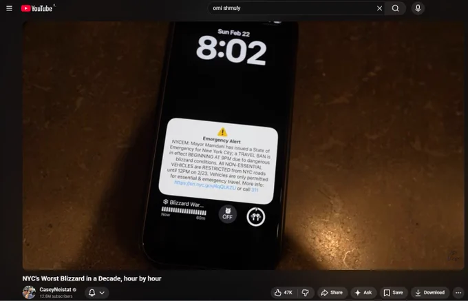 A screenshot from Casey Neistat's YouTube video titled "NYC's Worst Blizzard in a Decade, hour by hour." The image shows a smartphone displaying an "Emergency Alert" notification about a travel ban in New York City due to a blizzard, which is the exact sound and visual mentioned as a trigger for Israeli viewers.