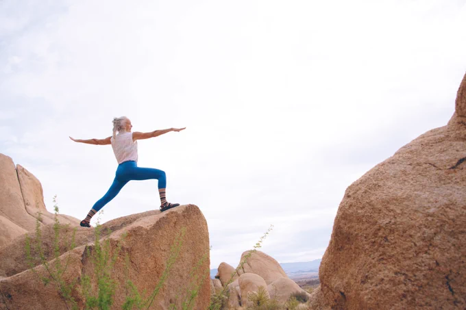 Older adult woman doing yoga on a rock formation.