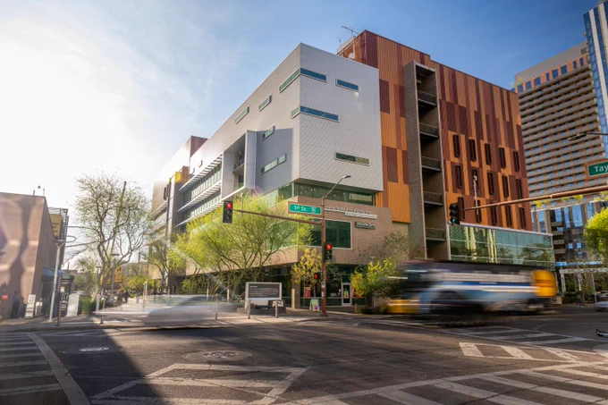 Modern multi-story building located on ASU Downtown Phoenix campus, with white and orange facade at a busy intersection under clear blue sky.