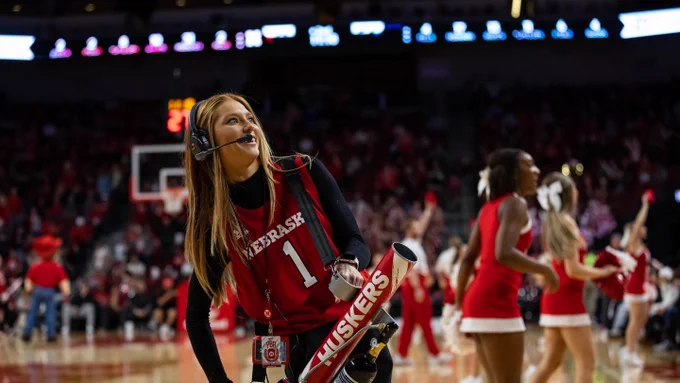 Female intern in Nebraska jersey fires t-shirts with a cannon into the crowd at a Husker basketball game