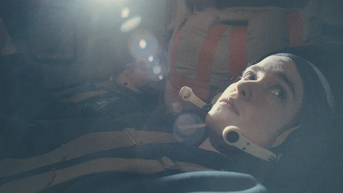 From Star City, Alice Englert as Anastasia Belikova is reclined wearing a space outfit looking up and off camera.