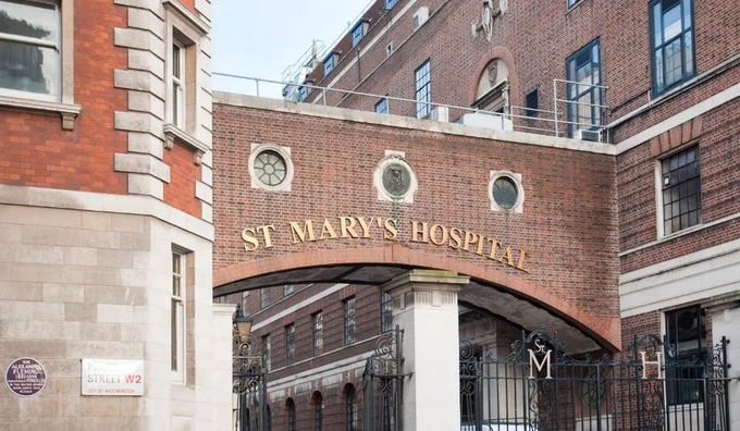 Entrance archway of St Mary's Hospital with gold lettering on red brick and wrought iron gates beneath.