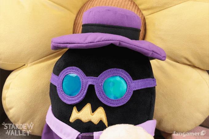 A photo of the head of the Incognito Krobus plush, showing its non-removable purple hat and glasses, as it reclines against a yellow cushion. 