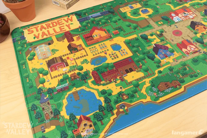 A photo of the Stardew Valley Pelican Town desk mat's upper left corner, showing the Stardew Valley logo and a colorful map of Pelican Town. 
