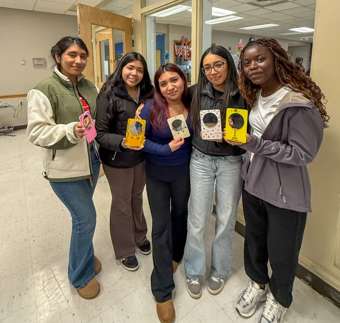 Five students stand together holding up mirrors they designed. 