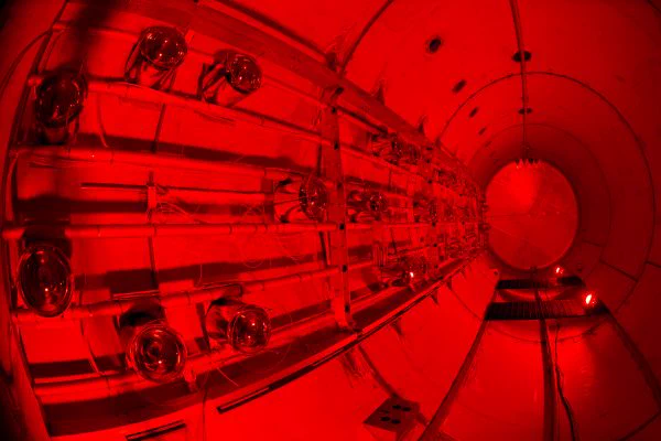 Inside view of the photomultiplier tubes on the MicroBooNE experiment at Fermilab. It is a long metal tube with instrumentation on the sides with red lighting. 