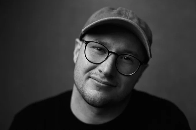 Black and white headshot of Jake Murtaugh wearing a baseball cap and glasses.