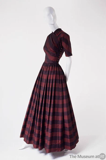 Full length view of the purple and red striped 1950s dinner dress by Claire McCardell showing how the fitted crossover bodice radiates out onto a long, full skirt