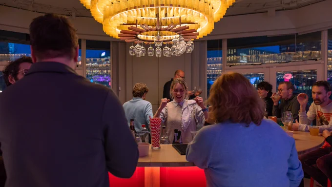 A woman standin in a round bar, holding her fists up from excitement. 