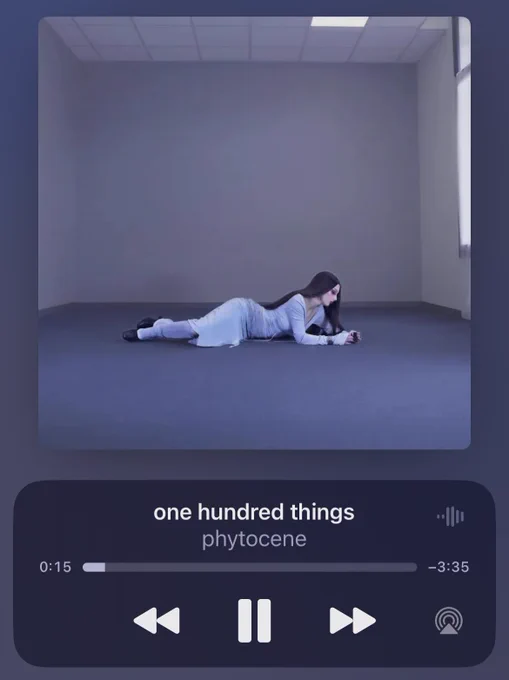 screenshot of the song playing on a streaming platform, with the single artwork displaying me, lying on the ground in an empty room with a blue floor and grey walls. i have long brown hair and i’m wearing a blue/grey top and skirt with black boots and blue/grey leg warmers. i’m looking at the ground, with a pensive expression on my face.