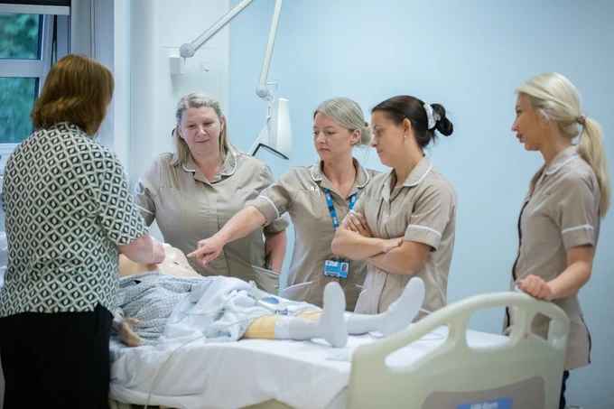 A group of nursing associate students standing around a hospital bed