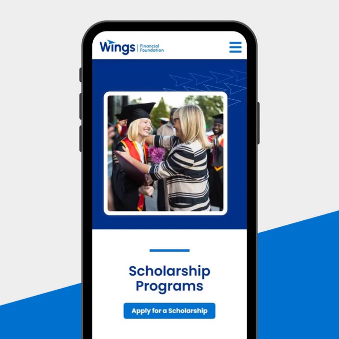 Image on a mobile phone displaying a Wings Financial advertisement featuring two individuals happily celebrating graduation, one in cap and gown, holding flowers. Text below reads 'Apply for a Scholarship'.