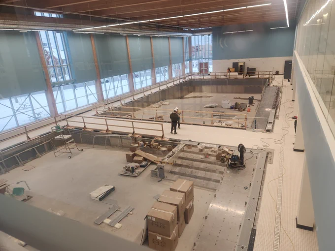 Inside of a building under construction with workers and building materials scattered around the empty pool area.