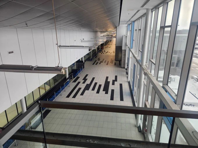 Long empty corridor in a modern building with large windows on one side and geometric black and white floor tiles.