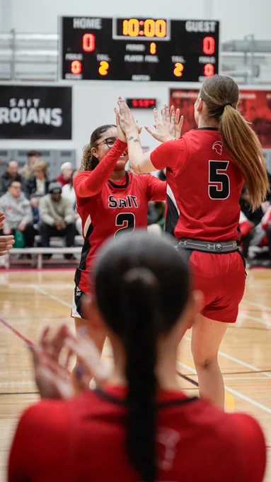 A SAIT Trojans basketball gives a high five to a teammate on the court.