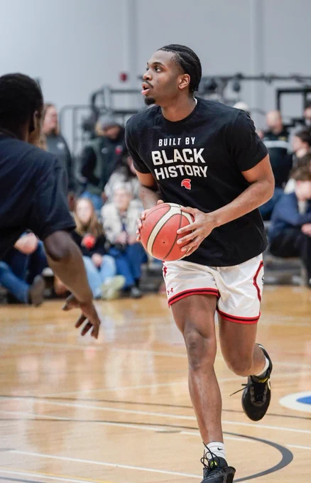 A SAIT Trojan is dribbling a basketball wearing a shirt that reads, "Built by Black History." 