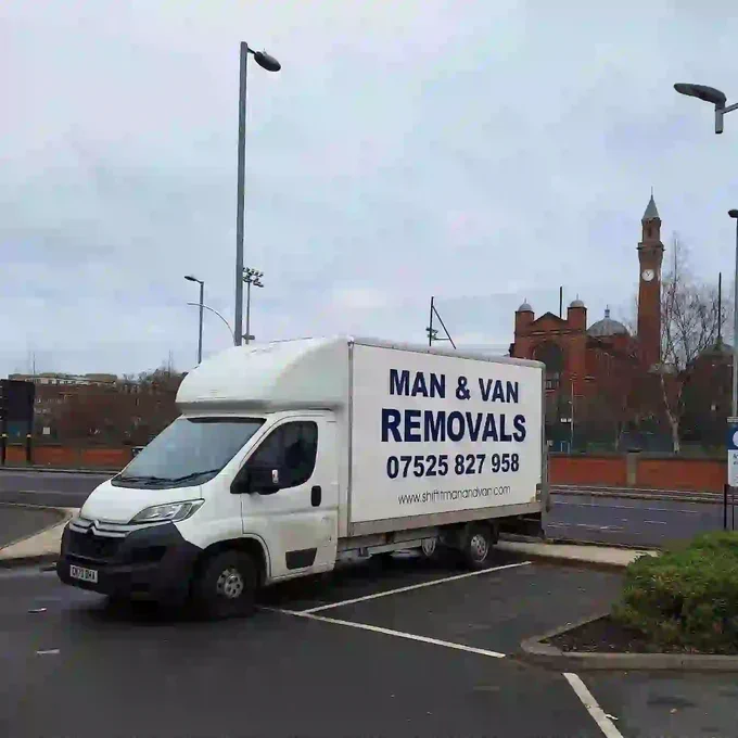 White removal Luton Van van parked in an empty lot with large "Man & Van Removals" lettering; red-brick clocktower building in the background which is Birmingham University 