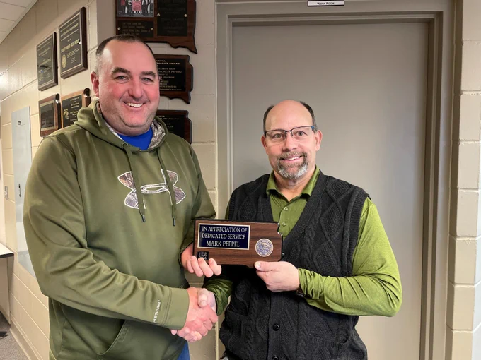 Two men in green posing in front of a 30 years of service award. 