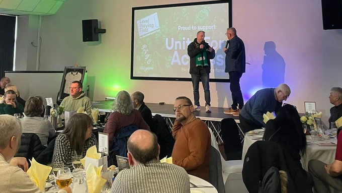 Level Playing Field's Daniel Townley, if in front of a screen with a 'Unite For Access' graphic on, being interviewed on stage in a hospitality suite, with people seated around tabled.