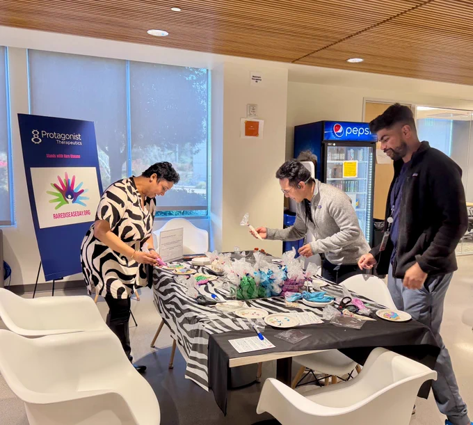 Three Protagonist employees gathered around a table that has a zebra-striped table cloth to decorate zebra-shaped cookies with icing