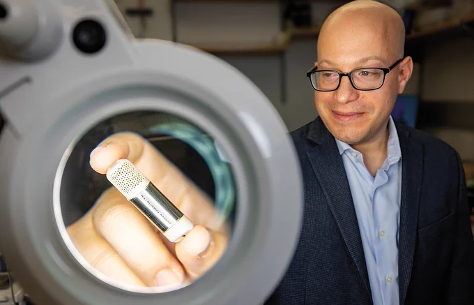Prof. Jonathan Rivnay holds his implantable device in front of a magnifying glass
