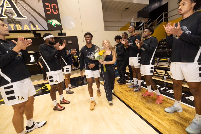 Senior Donovan Vickers and his fiancee walk onto a basketball court. Parallel lines of teammates on each side of them. Vickers holds flowers. 