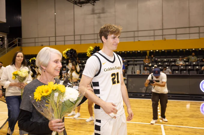 Jordan Hansen and his family walk through a basketball court. Two women behind him hold flowers. 