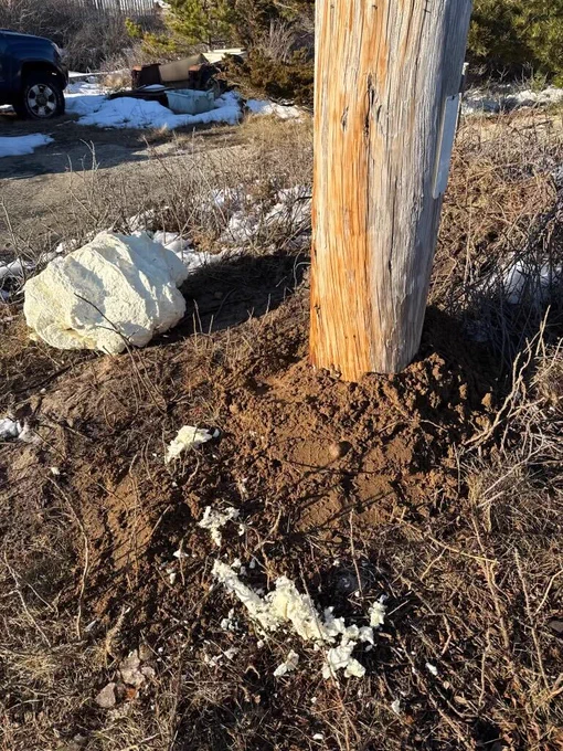 Close-up of the base of a wooden utility pole surrounded by disturbed soil.