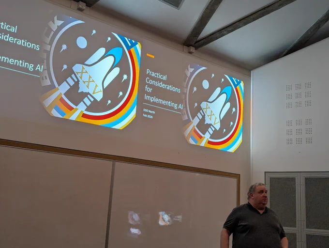 Robert Hogg, bottom right of picture, presenting at DDDNorth at the University of Hull, with his opening slide on dual screens behind him.