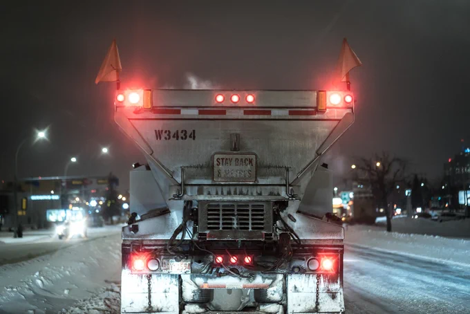 A City of Edmonton snow plow travels a city road at night.
