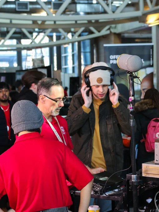 A lively event at SAIT, featuring a person in a hat wearing headphones at a try-a-skill activity. Numerous attendees and banners are visible in the background.