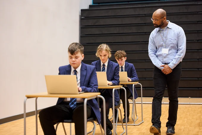An invigilator and three students sitting digital exams in an exam hall. 