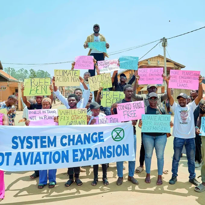 Young people holding banner system change not aviation, as well as several placards against aviation and oil