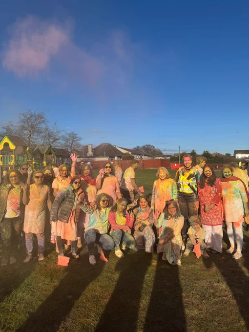 Female police officer and members of the public in a park covered in colourful powder.