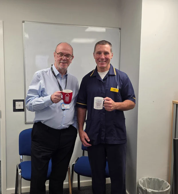 Sir David Nicholson KCB CBE, Group Chair and Andy Tams Undergraduate Medical Education Team (UMET) Manager/Advanced Nurse Practitioner at Walsall Healthcare, are seen holding mugs while standing together in an office setting. They recently met to catch up, discussing their career paths and their roles within healthcare.