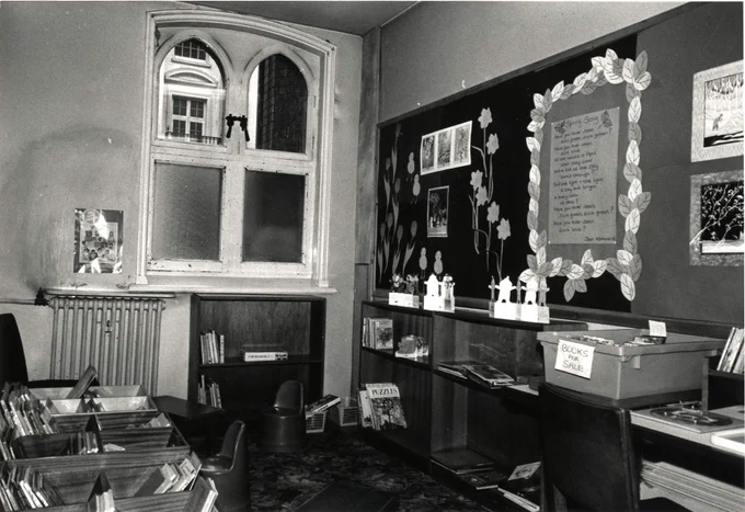Black and white photo of Reading Central Library, Blagrave Street. The Children's Library, 1985. There are kinder boxes to the left, and there is a decorative mural display on the subject of spring to the right of the window.