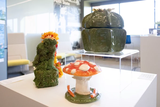 Three earth-based sculptures that feature a mushroom, and mossy grass and flowers.