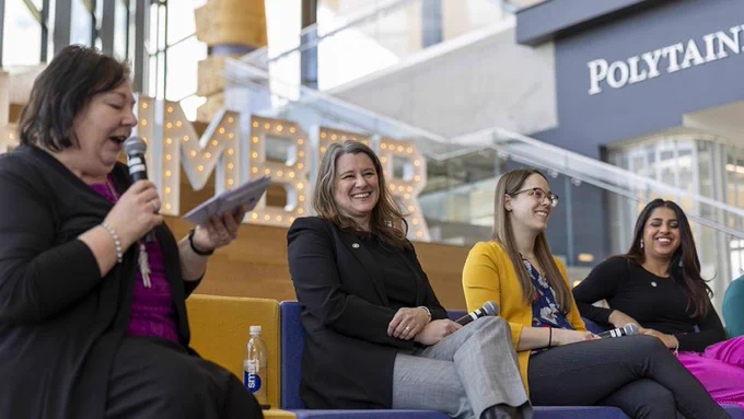 Several people on a stage are sharing a laugh while the moderator speaks into a microphone.
