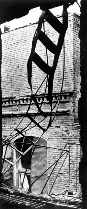 The flimsy fire escape ladder descended close to the building forcing those fleeing to struggle through flames and past warped iron window shutters stuck open across their path. Sections of ladder which ended two stories above the ground, twisted and collapsed under the weight of workers trying to escape the fire killing many who had chosen it as their lifeline.