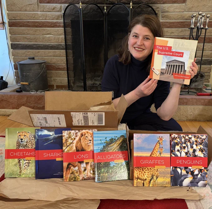 Author Andrea MacDonald holds a copy of her new book, a guide for middle-grade students called The U.S. Supreme Court. In the foreground are six other books she recently co-authored. The books in front are from a  series on wild animals called Odysseys.
