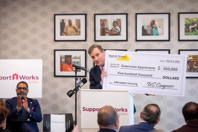 U.S. Sen. Mark Warner at podium holding oversized $500,000 check for Greenview Apartments affordable housing funding announcement.