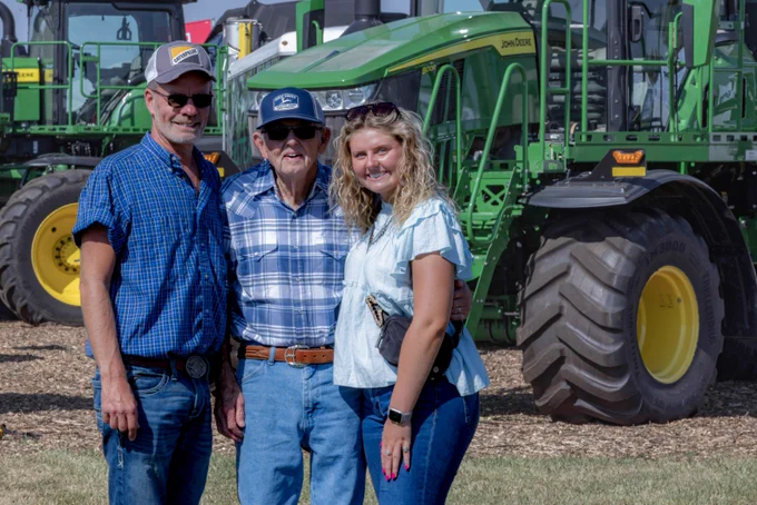 Three Farm Science Review attendees smile and pose for a picture in front of a green tractor.
