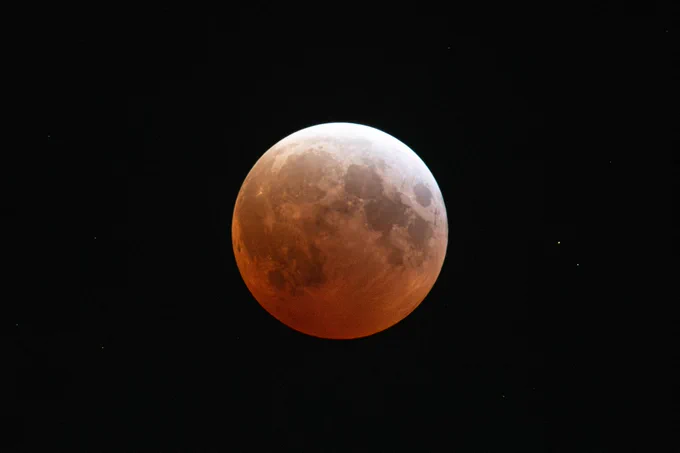 A blood moon is centered in the image, illuminating the sky in shades of red and orange. Credit: NASA/Jordan Cochran