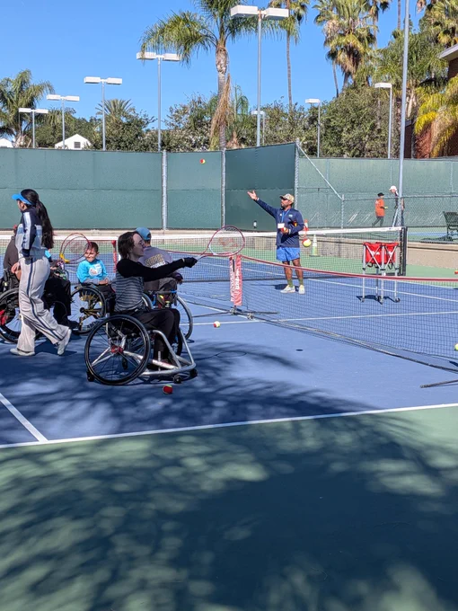 Wheelchair user in a sports chair holding a tennis racket on a tennis court 